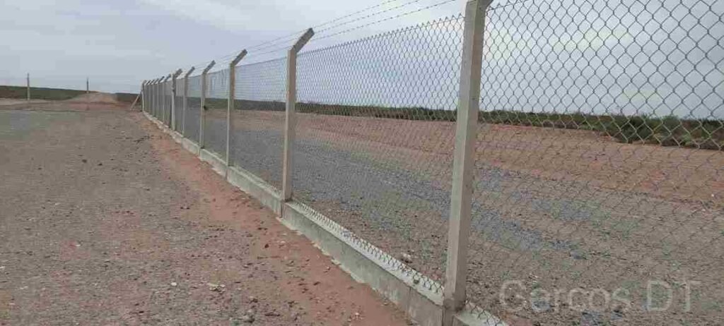 Instalación de alambrado olímpico de alta seguridad con postes de hormigón reforzado, brazo de extensión y tres hilos de alambre de púas en un predio logístico de Neuquén Capital, Alto Valle.